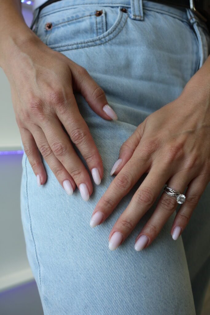 Close-up of soft pink builder gel manicure Tampa with elegant hands resting on denim.
