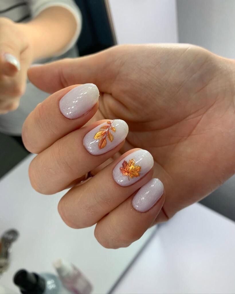 Soft white nails with golden autumn leaves created by european manicure in Tampa.
