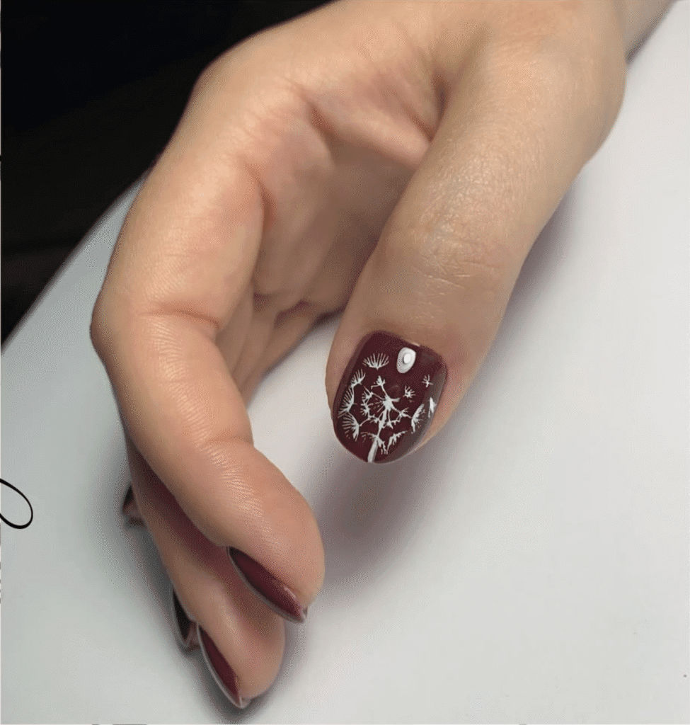 Hand with burgundy polish and white floral art created with russian nail salon technique in Tampa.