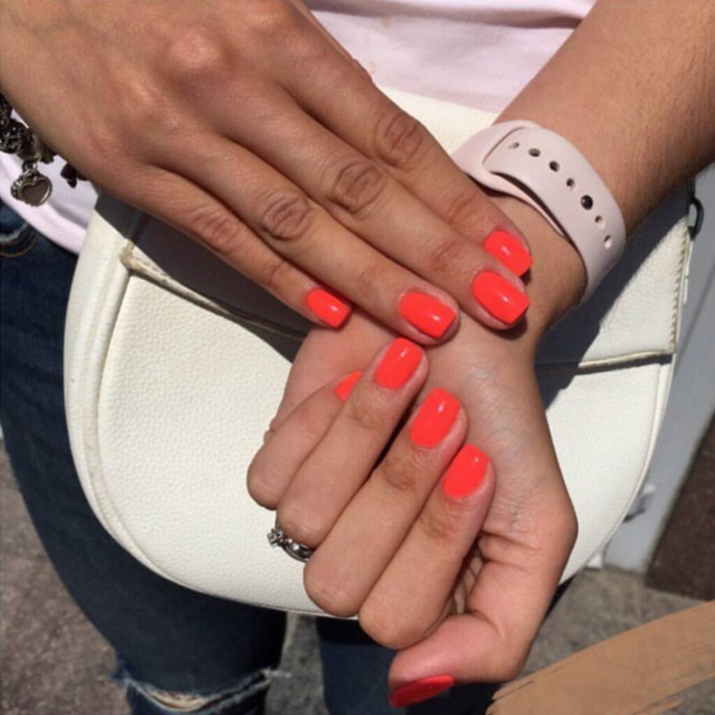 Bright neon coral russian Nails Tampa manicure on well-groomed hands in Tampa, Florida sunlight.