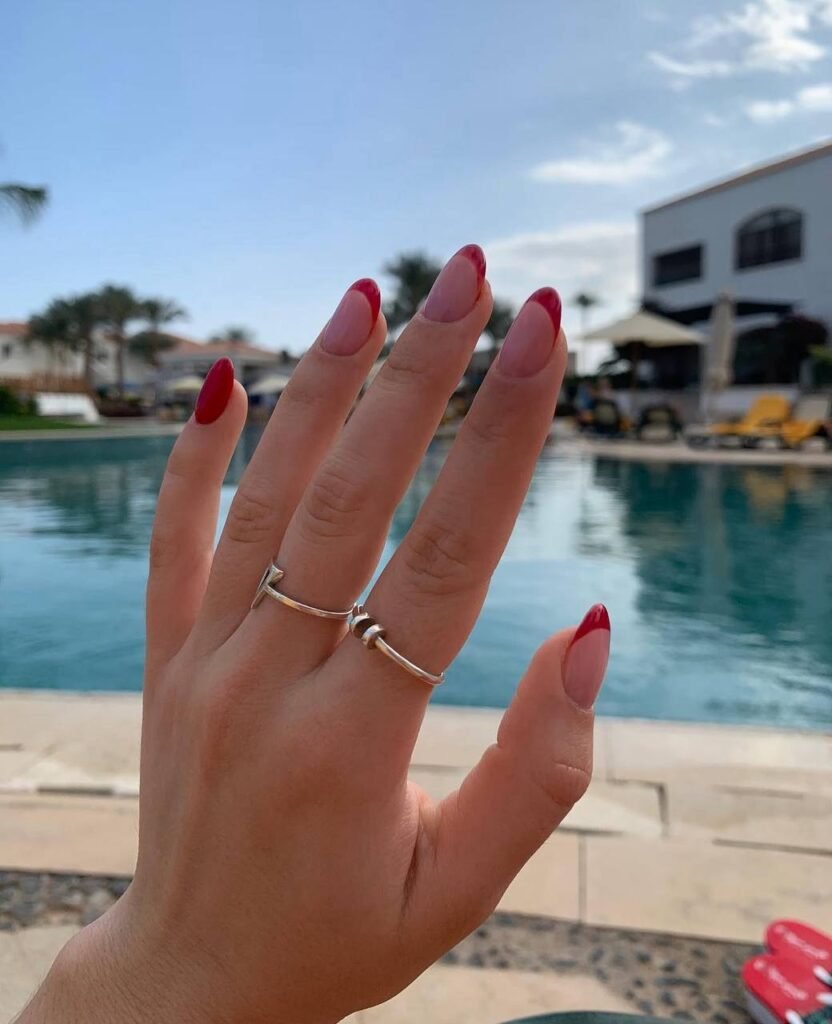 Hand with red French tip hard gel russian manicure in Tampa by a pool under natural sunlight