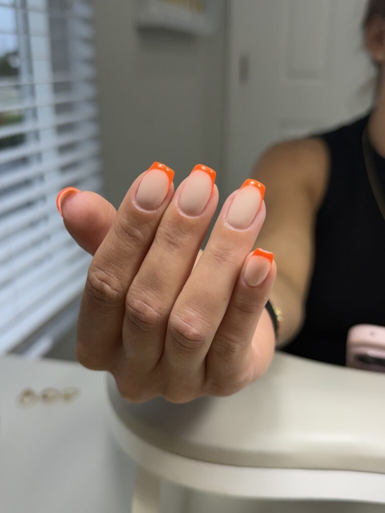 Elegant russian manicure with nude nails and vibrant orange French tips at Nail Boss Studio Tampa, Florida.