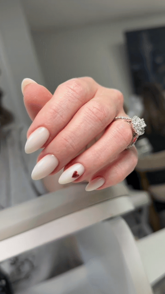 Milky white almond-shaped nails with a tiny red heart accent at a russian manicure salon in Tampa, Florida.