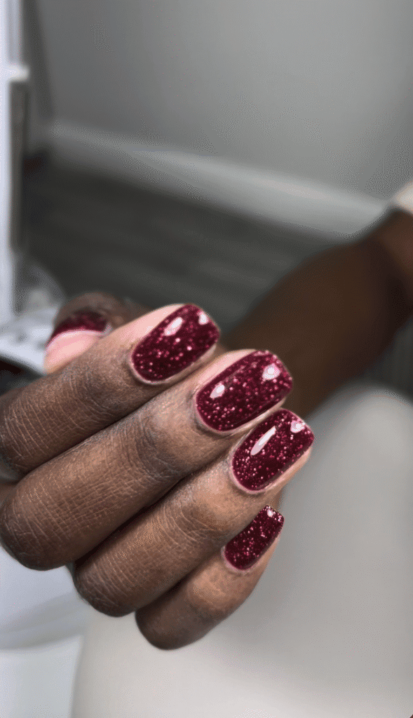 Glossy burgundy glitter russian nails Tampa manicure on deep skin tones, featuring sparkling ruby polish and softly squared nails.