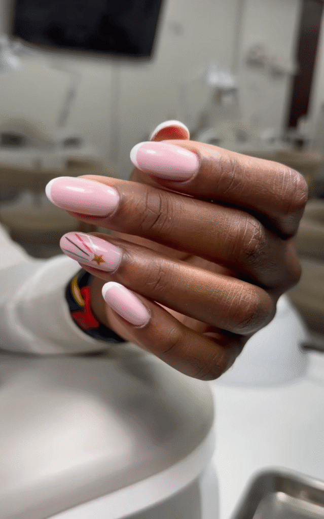 Soft pink builder gel manicure in Tampa featuring almond nails, white French tips, delicate line art, and a gold star accent.